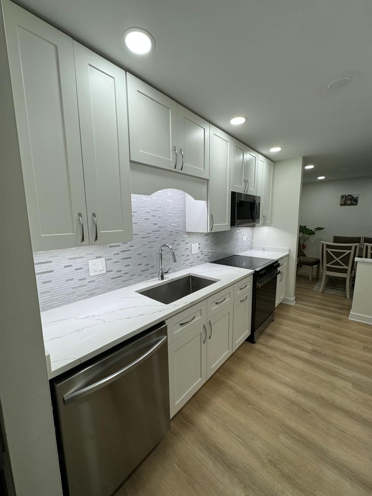 Remodeled kitchen with white shaker cabinets, white countertops, undermount sink and mosaic tile backsplash